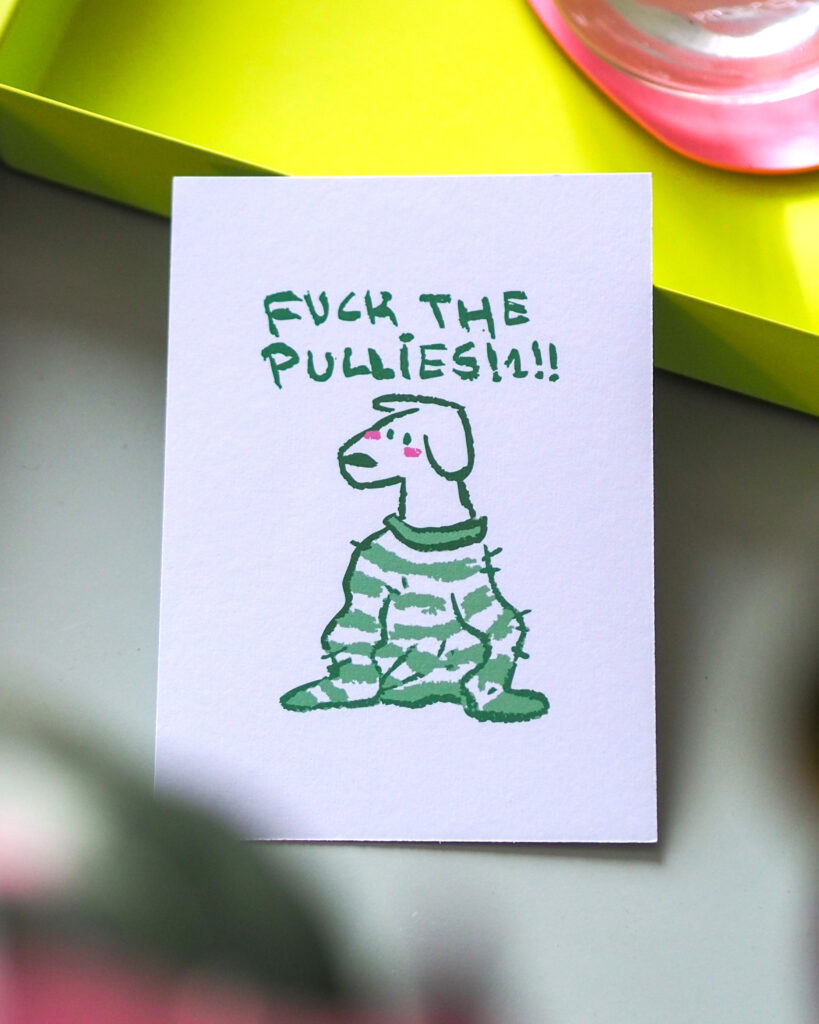 Foto der Postkarte "F*ck the Pullies" mit einem Hund der einen zu großen Pullover trägt